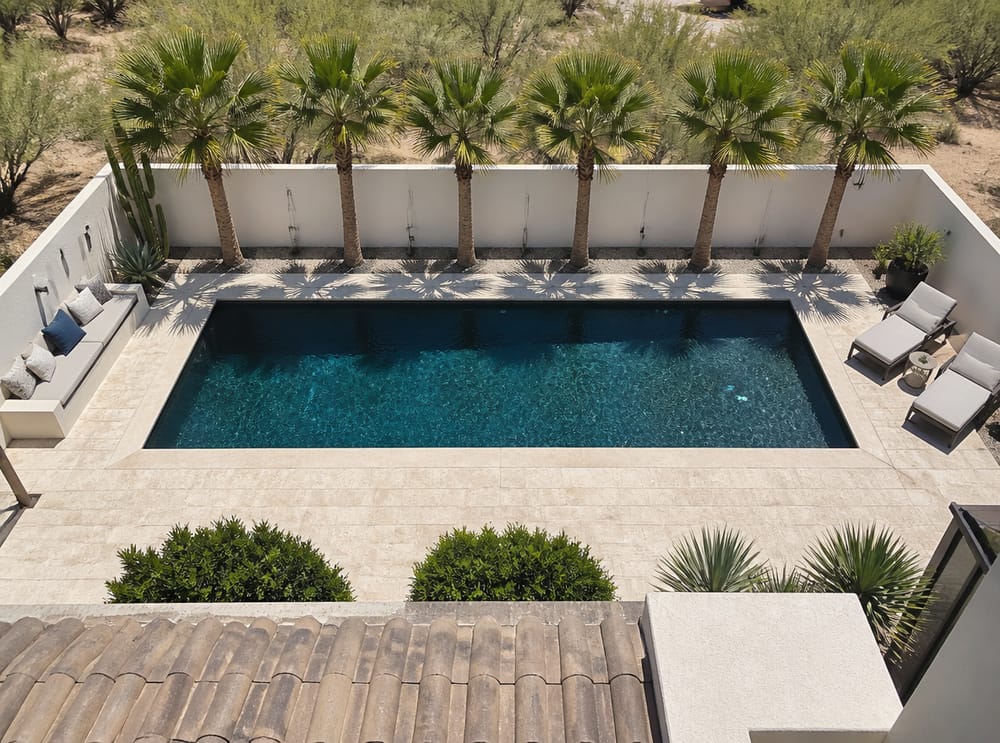 Alberca rectangular con deck de travertino y palmeras