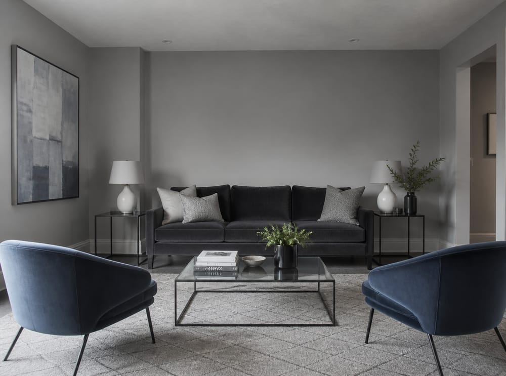 Tonal grey-on-grey room, blue accent chairs, glass table