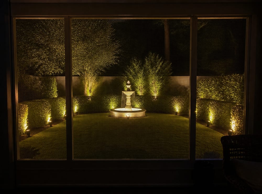 Backyard uplights and fountain viewed through screen porch