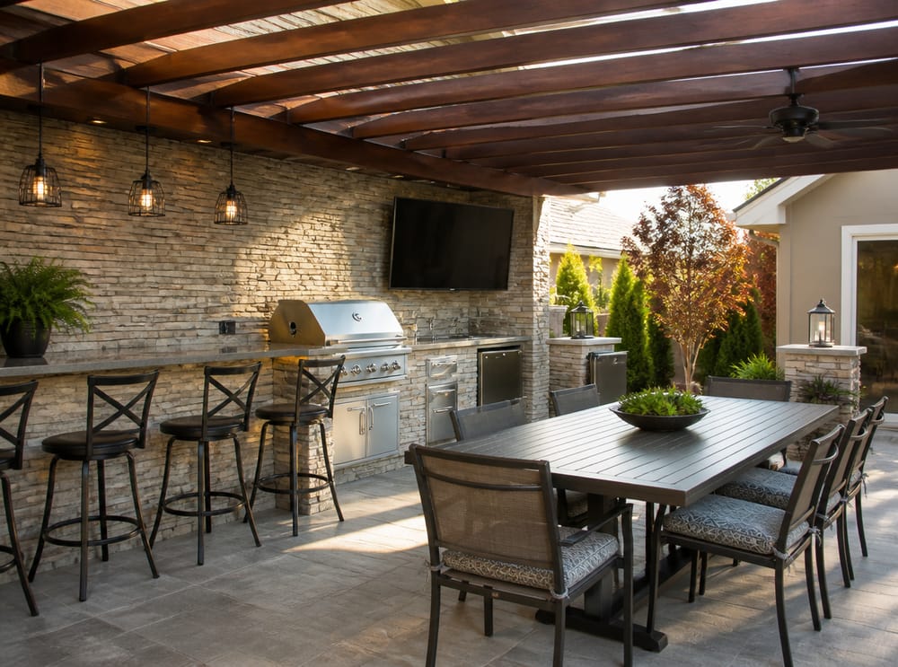 Cucina outdoor in pietra con sgabelli e zona pranzo sotto pergola